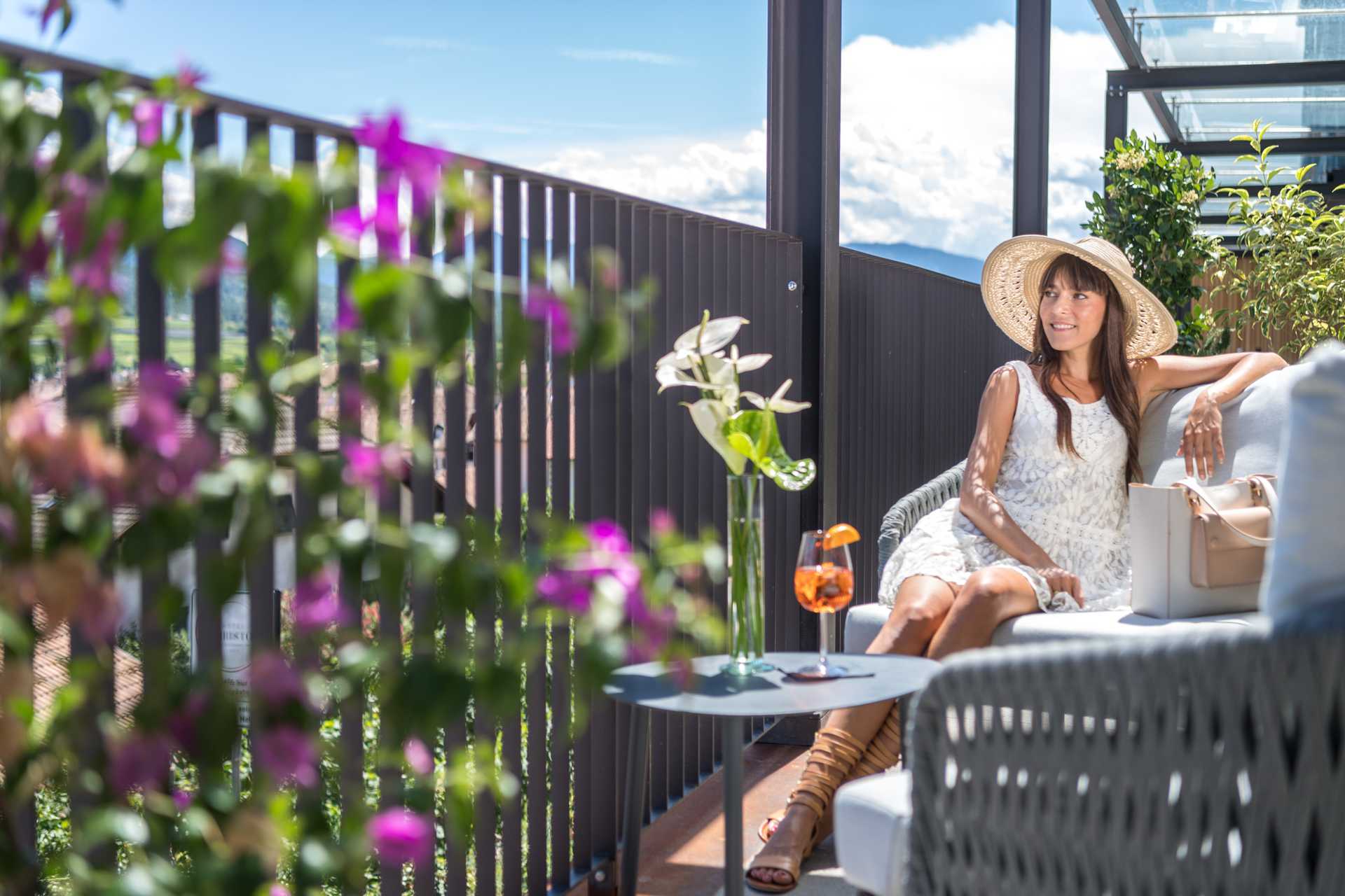 Arrive and relax, recover, switch off Woman sits in the lounge outdoor area and enjoys the sun with a drink.