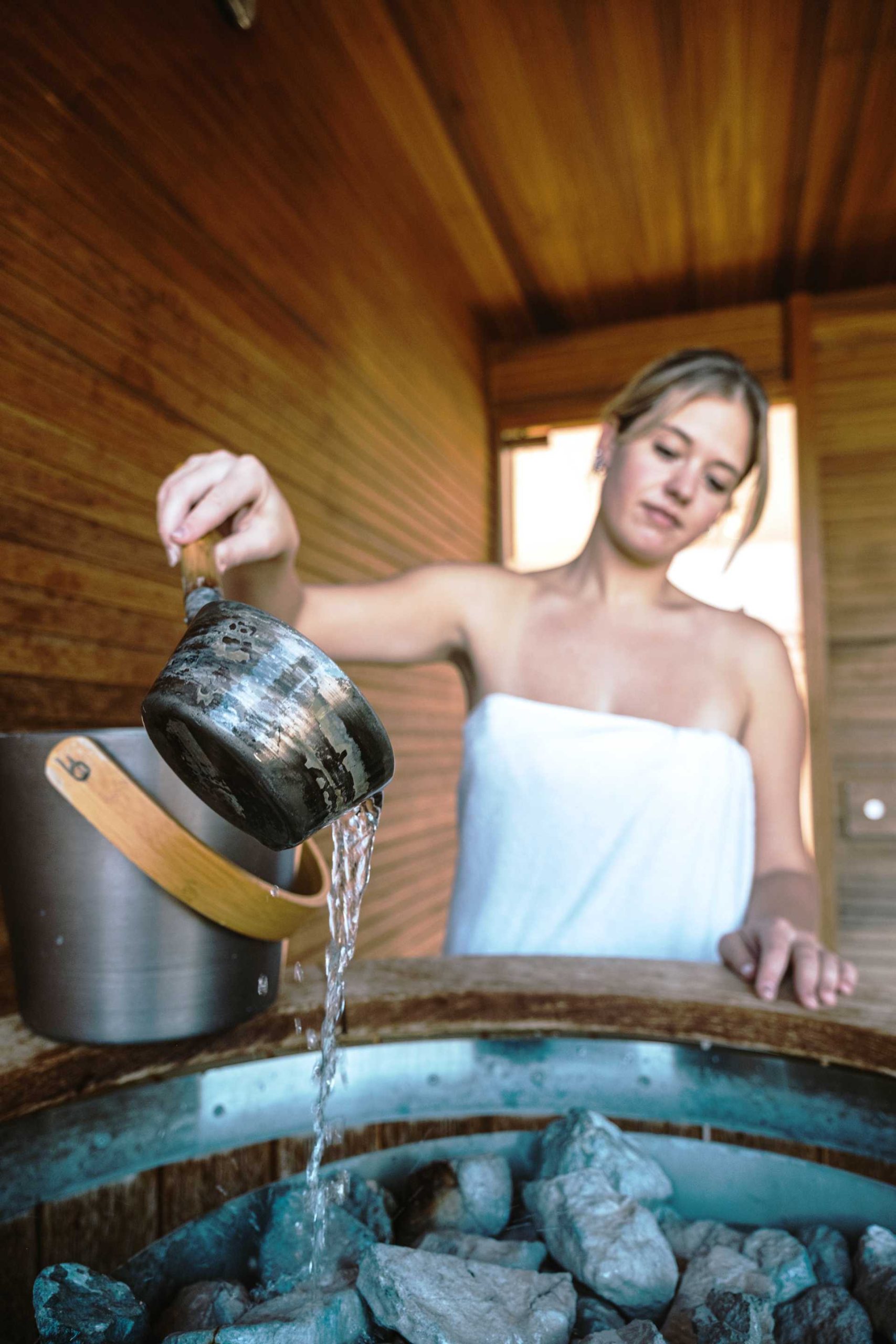 eine Frau macht sich selber einen Aufguss in der Sauna